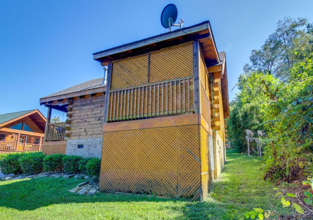 Modern log cabin featuring warm wood construction with private balcony, nestled among mature trees in a peaceful residential setting.
