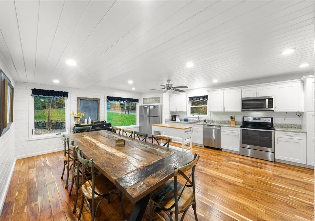Gather around the rustic farmhouse table in your bright, open kitchen where wide windows frame peaceful garden views, making every meal feel like a country escape.