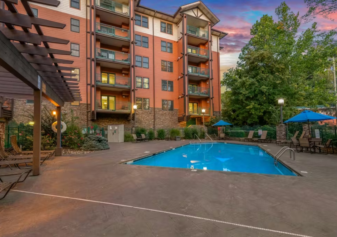 Baskins Creek with outdoor pool surrounded by lush trees and colorful sunset sky.