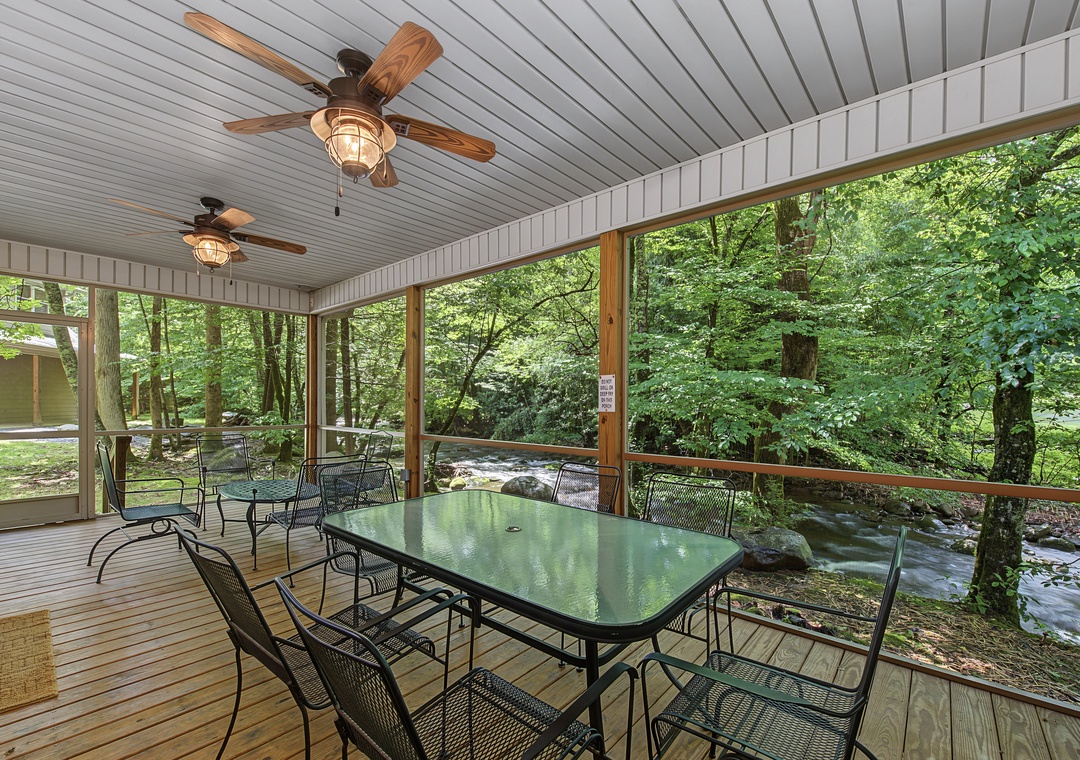 Picture yourself dining under rustic ceiling fans as a gentle stream flows just beyond the screen. This covered porch invites you to unwind with morning coffee or evening meals, cooled by the breeze and soothed by nature's soundtrack.