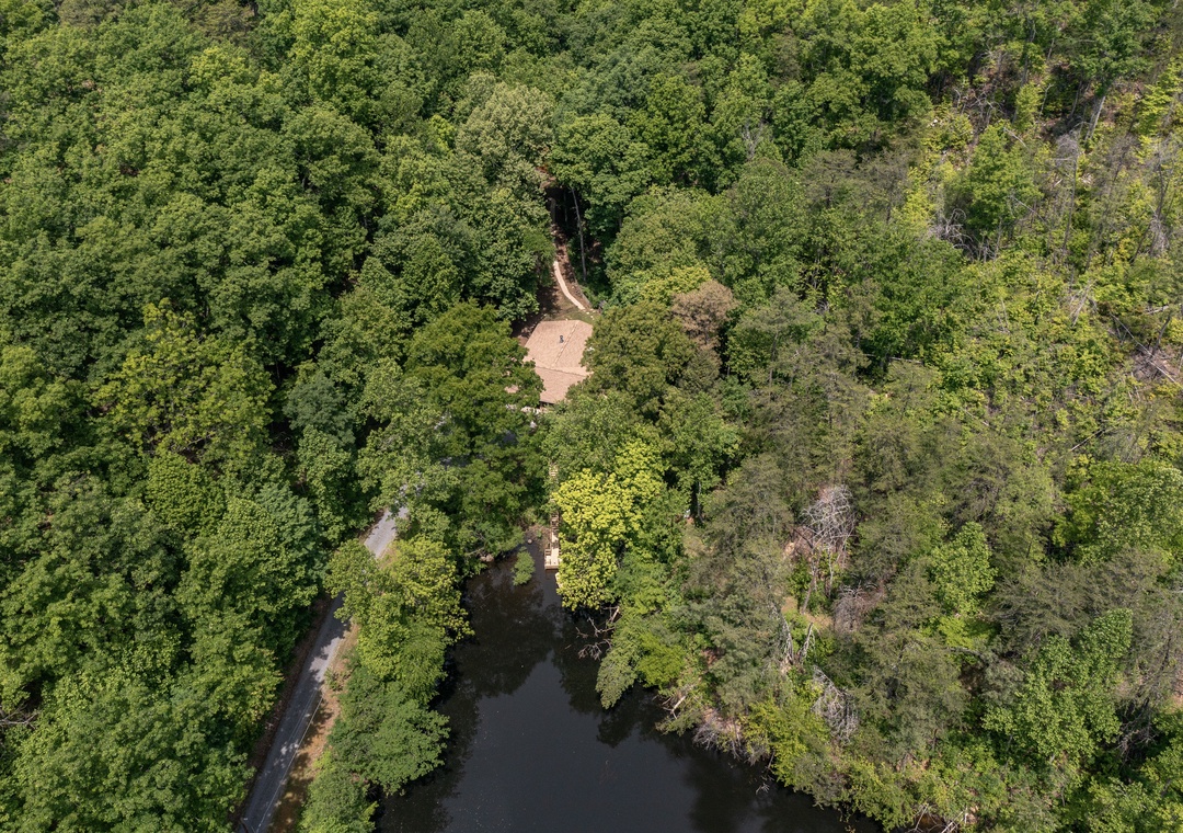 Aerial view capturing the property nestled within a lush, forested landscape, showcasing its secluded natural surroundings and tranquil woodland setting.