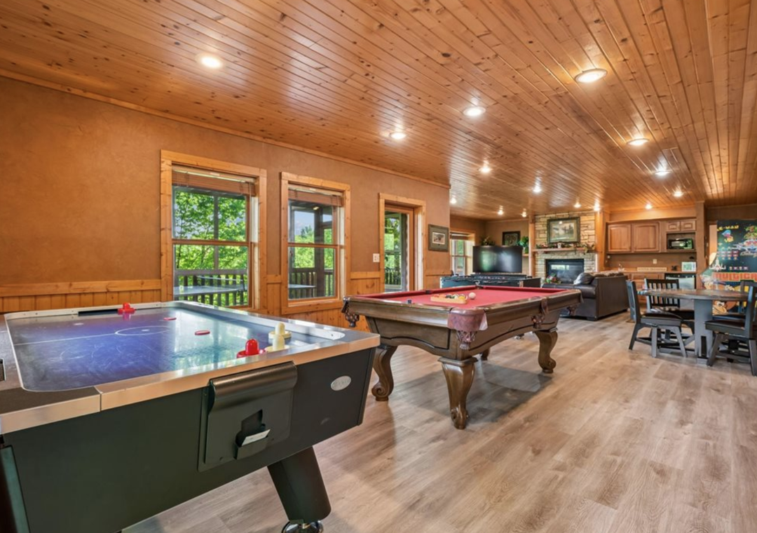 Your own private game room with air hockey, billiards, TV, and dining—perfect for family fun or friendly competition under warm wood ceilings and natural light.