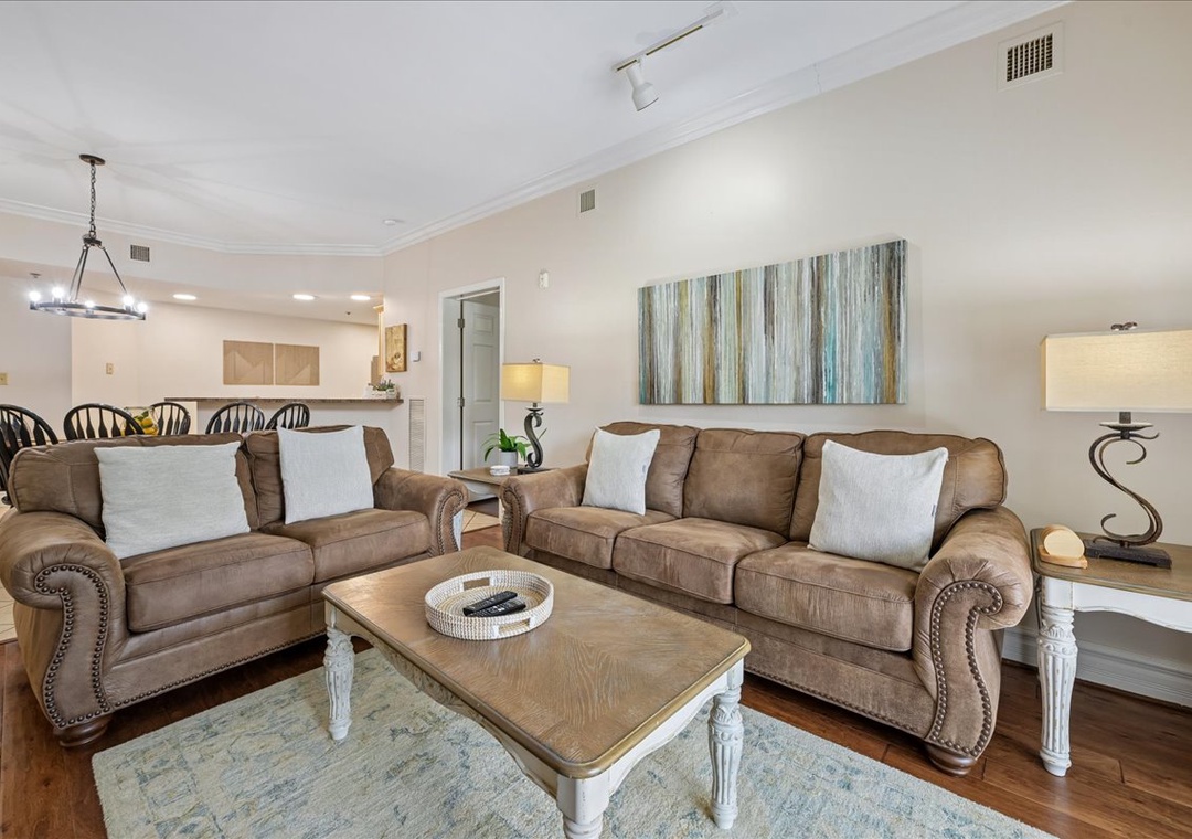 Relax in your spacious living room featuring plush leather seating, elegant lighting, and coastal artwork that creates the perfect atmosphere for unwinding after beach adventures.
