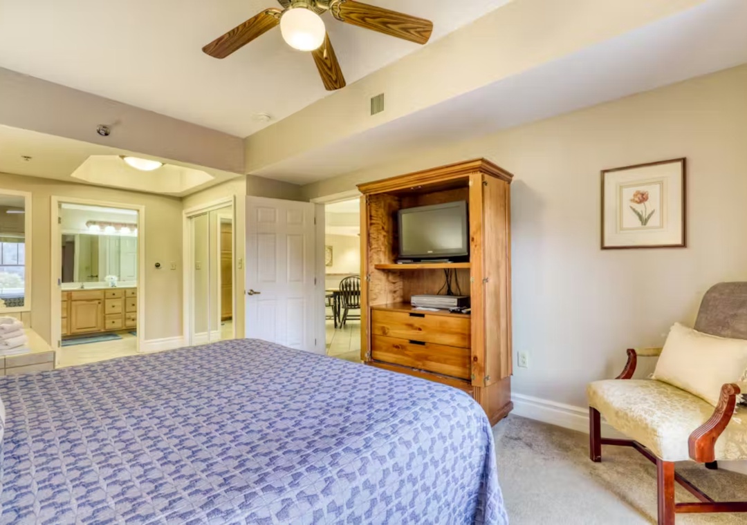 Relax in your spacious master suite with cozy seating, wood entertainment center, and ceiling fan for comfort.
