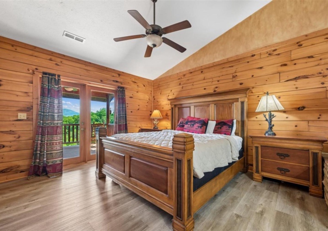 Drift off in your cozy cabin retreat with warm pine walls, a plush bed, and stunning mountain views just beyond the balcony doors—your perfect mountain escape awaits.