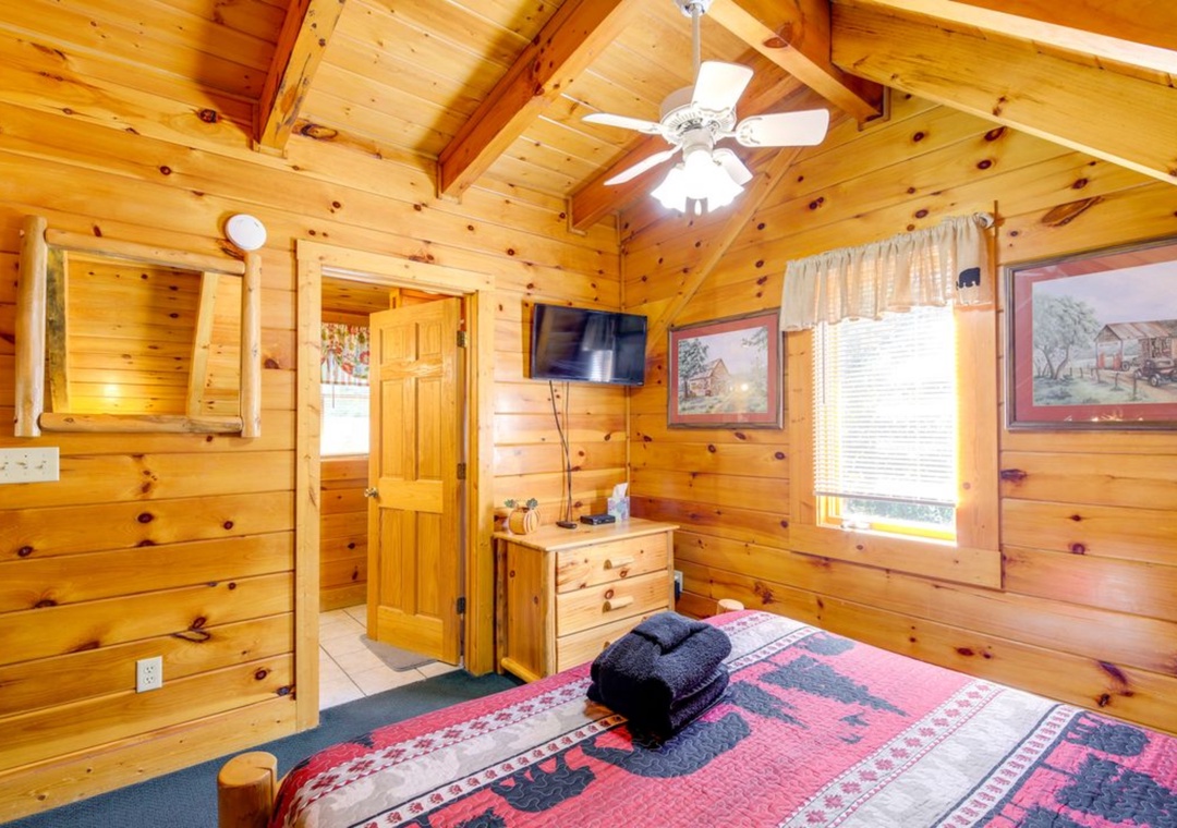 Cozy log bedroom with knotty pine walls, ceiling fan, and rustic charm for your mountain getaway.