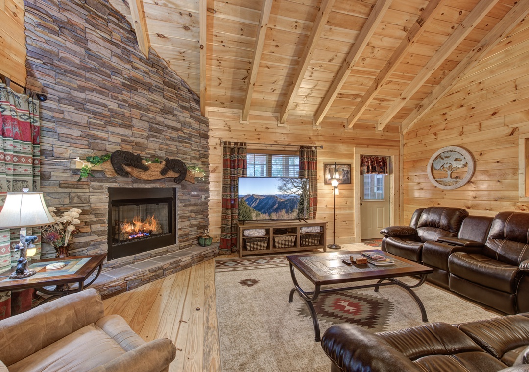 Unwind by your crackling stone fireplace in this cozy living room with leather seating and rustic wood-beam ceiling warmth.