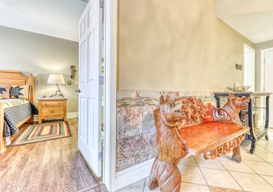 Step into your cozy retreat featuring an ornate wooden bear bench and fireplace, with rustic bedroom charm just steps away.