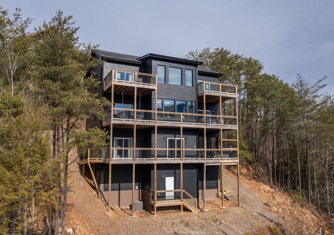 Modern lakeside retreat featuring multiple levels of outdoor decks and balconies surrounded by wooded natural landscape.