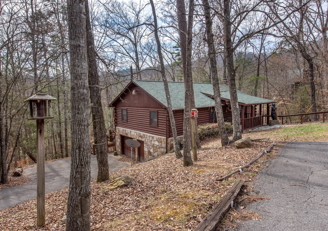 Rustic log cabin nestled among towering trees with stone accents and covered deck, perfectly situated on a peaceful wooded street.