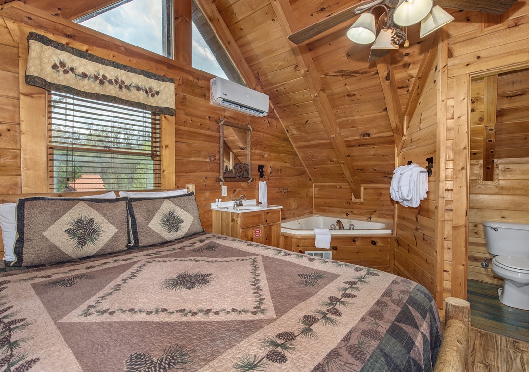Your cozy cabin bedroom features rustic wood walls, pinecone-themed bedding, and a relaxing jetted tub for ultimate comfort.