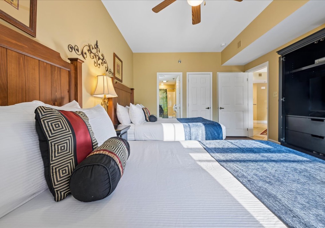 Sink into plush bedding with decorative pillows in your spacious bedroom, featuring warm wood accents and modern TV entertainment.