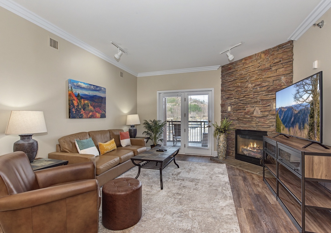 Unwind in your spacious living room featuring rich leather seating, a cozy stone fireplace, and large TV for perfect evening relaxation.