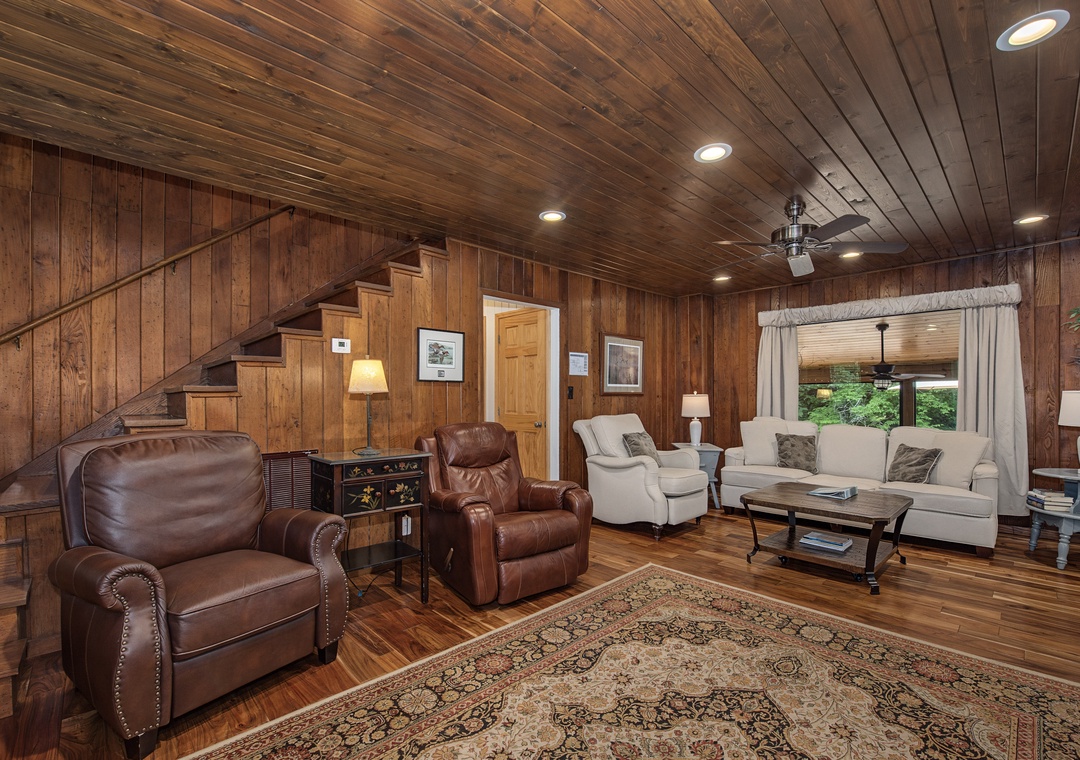 Step into your own rustic retreat, where warm wood-paneled walls and plush leather seating invite you to unwind. A large window frames peaceful greenery, filling the space with natural light and mountain charm.