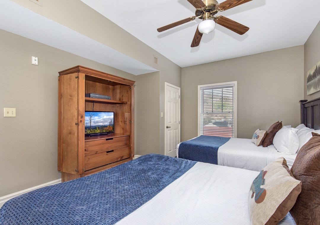 Unwind in your comfortable bedroom with two queen beds, featuring a warm wood entertainment center and ceiling fan for perfect comfort.