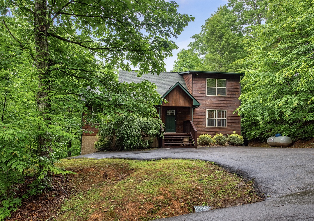 A charming wooden cabin nestled among lush trees, offering a peaceful retreat with ample parking and private outdoor space surrounded by nature.