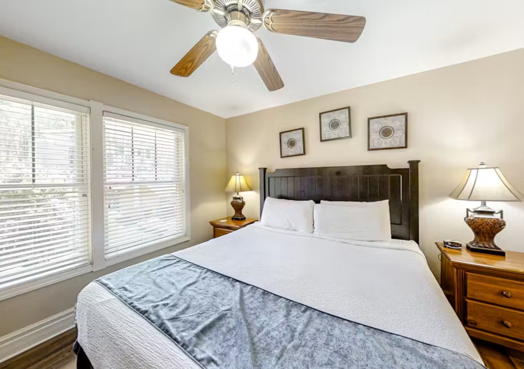 Sink into crisp white linens in your peaceful bedroom, where warm lighting and a gentle ceiling fan create the perfect atmosphere for rest.