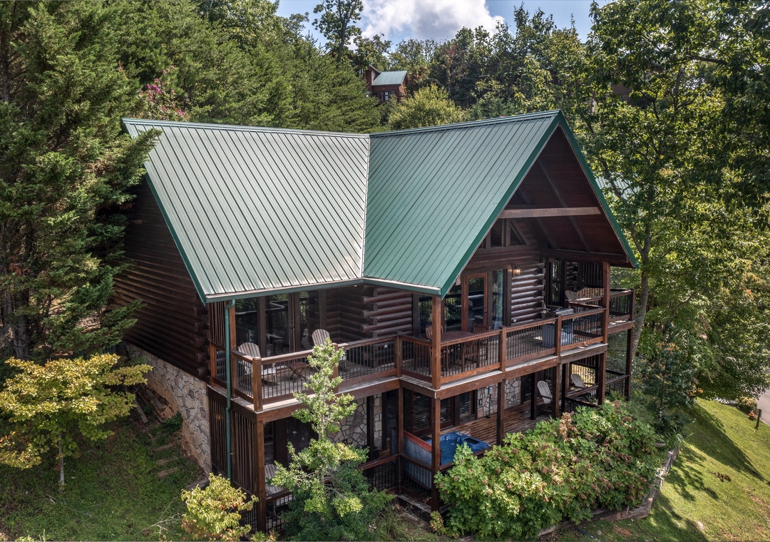 Rustic log cabin nestled among towering trees with expansive wraparound decks and natural forest surroundings.