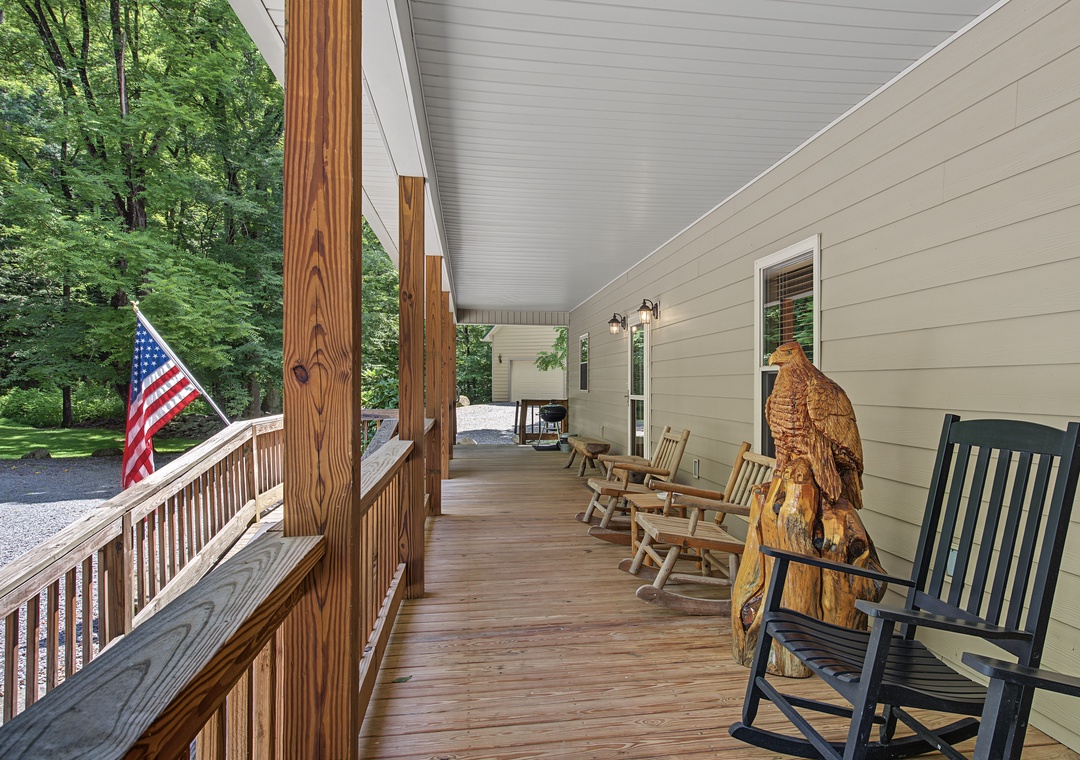 Covered porch framed by lush wooded surroundings, featuring cozy rocking chairs for relaxing mornings and a carved wood accent for rustic charm.