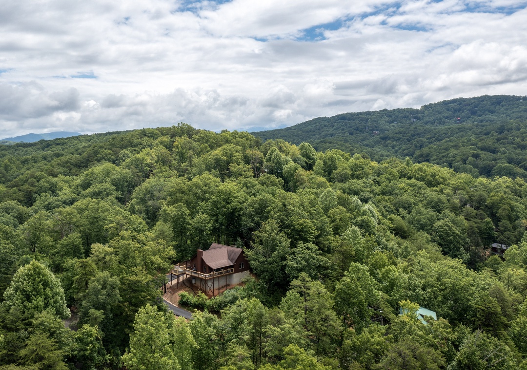 A secluded mountain cabin nestled among lush green forests, offering tranquil privacy and breathtaking views of rolling, tree-covered hills beneath a dramatic sky.