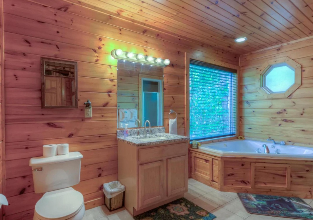 Unwind in your private spa-like bathroom with a deep soaking tub, warm wood paneling, and natural light streaming through the window—your perfect mountain retreat sanctuary.