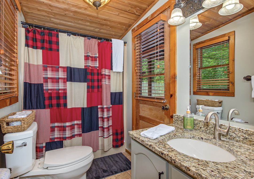 Step into your private bathroom with its warm wood-beam ceiling and granite vanity. Fresh towels, a charming quilted curtain, and peek-a-boo forest views through the window make this rustic retreat feel like home.