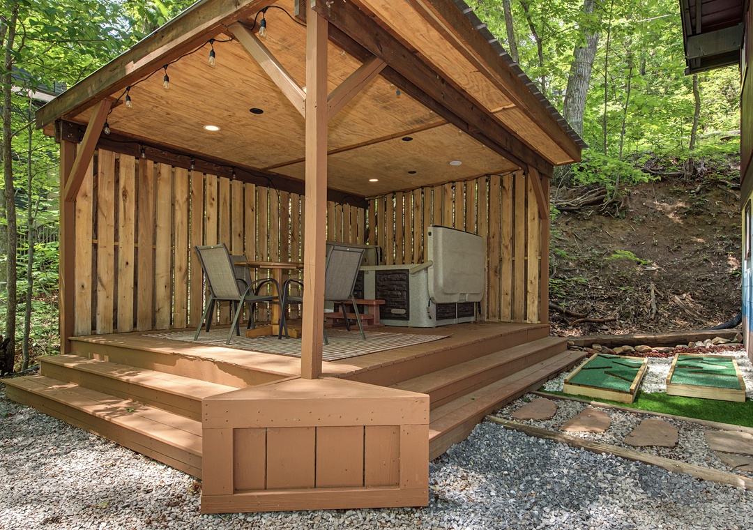 A charming open-air pavilion nestled among mature trees, featuring a miniature golf green and comfortable seating for outdoor relaxation and fun.