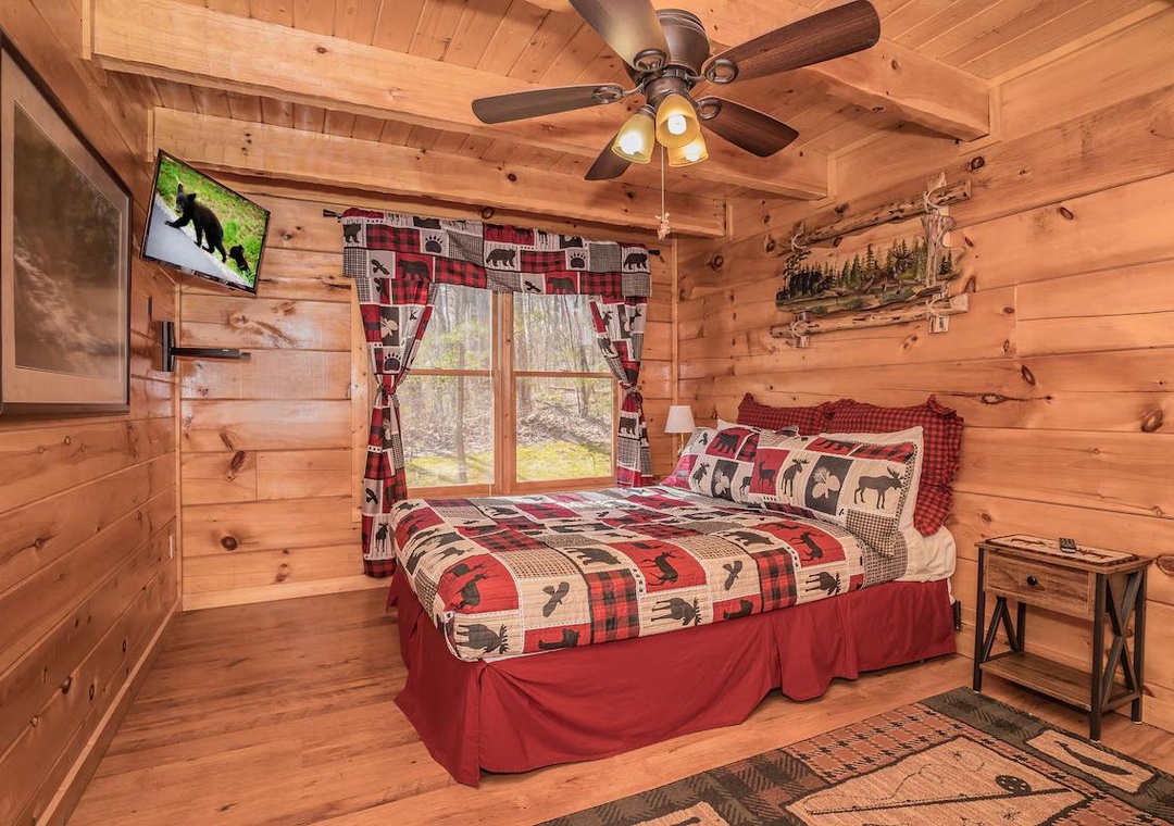 Cozy up in your rustic cabin bedroom with warm wood walls, themed bedding, and a ceiling fan for comfort.