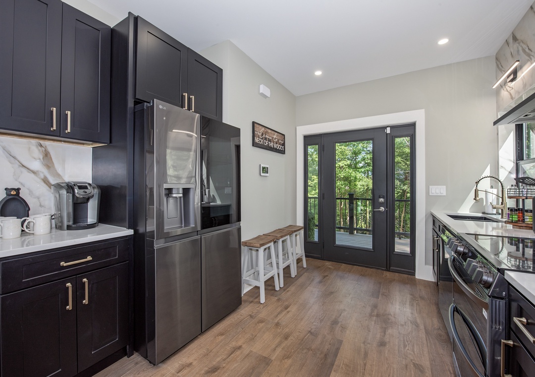 Your modern kitchen features sleek cabinetry, stainless steel appliances, and natural light from doors opening to a private deck with wooded views.