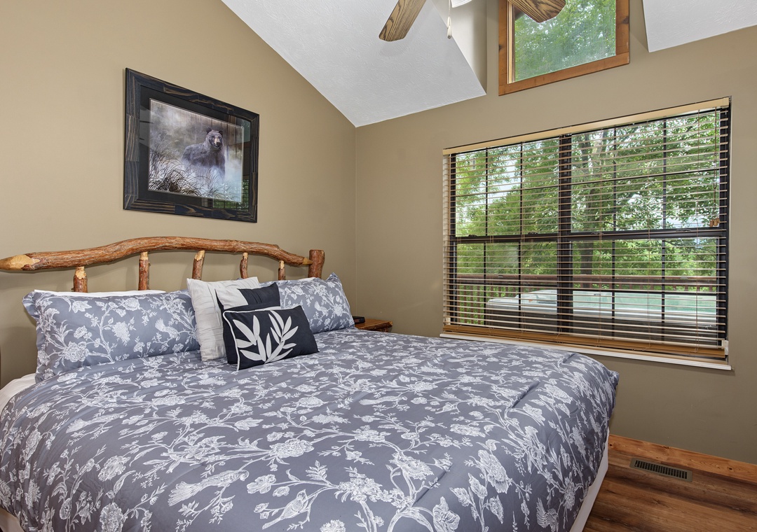 Drift off to sleep in your cozy bedroom, where natural light streams through skylights and windows framed by lush forest views. The rustic wood headboard and soft linens create a peaceful mountain retreat.