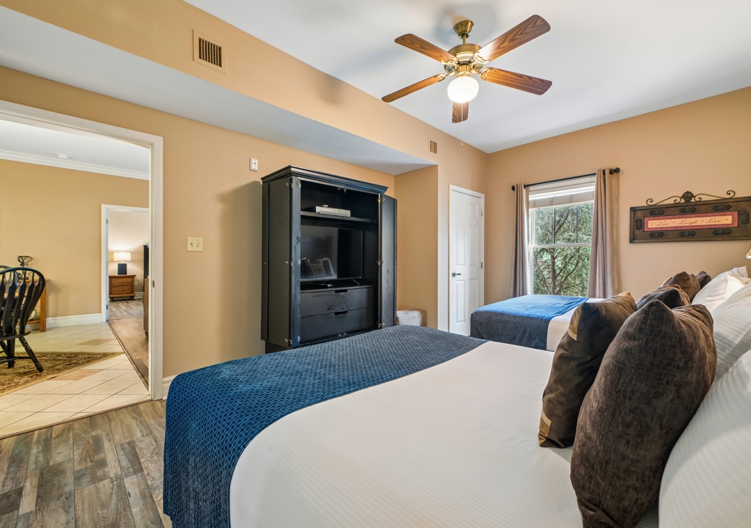 Relax in your spacious bedroom featuring twin beds with plush linens, ceiling fan, and entertainment center for cozy evenings.