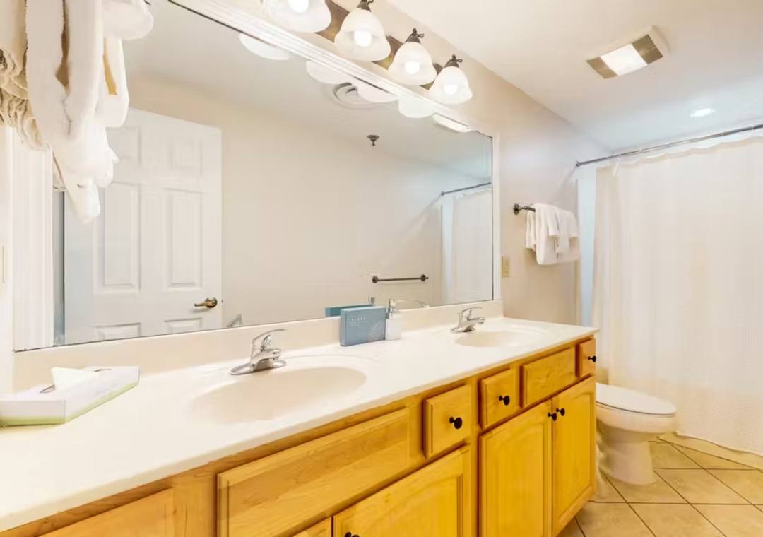 Step into your spacious bathroom with dual sinks, warm wood vanity, and fresh towels awaiting your arrival.