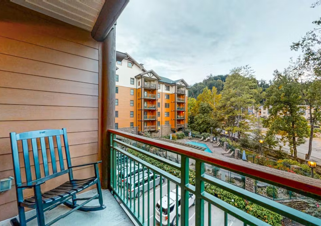 Relax in your rocking chair on this peaceful balcony, taking in views of charming buildings and lush trees below.