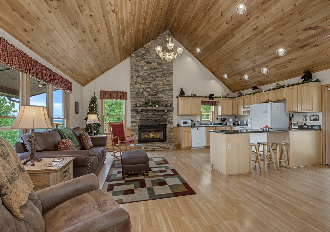 Relax in your open-concept cabin featuring vaulted wood ceilings, a cozy stone fireplace, plush seating, and a fully equipped kitchen—perfect for mountain getaways.