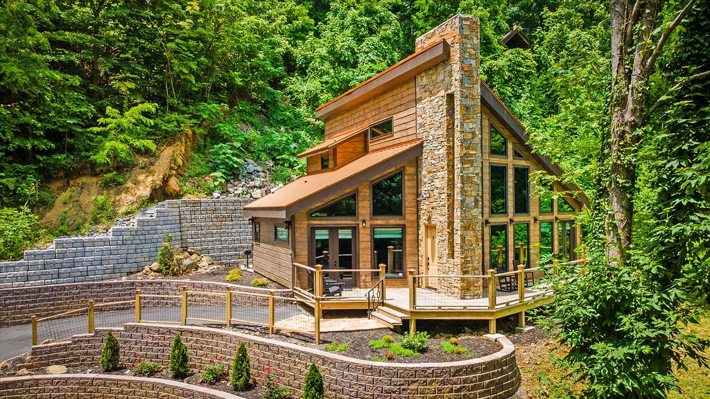 Nestled in lush greenery, this stunning cabin blends rustic warmth with modern design, featuring a striking stone chimney and expansive windows that invite nature inside.