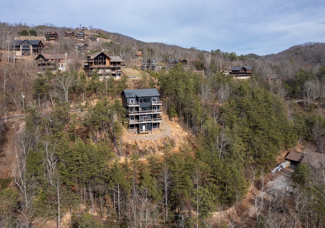 Aerial view of mountain cabin development nestled among forested hills with multiple vacation properties scattered throughout the landscape.