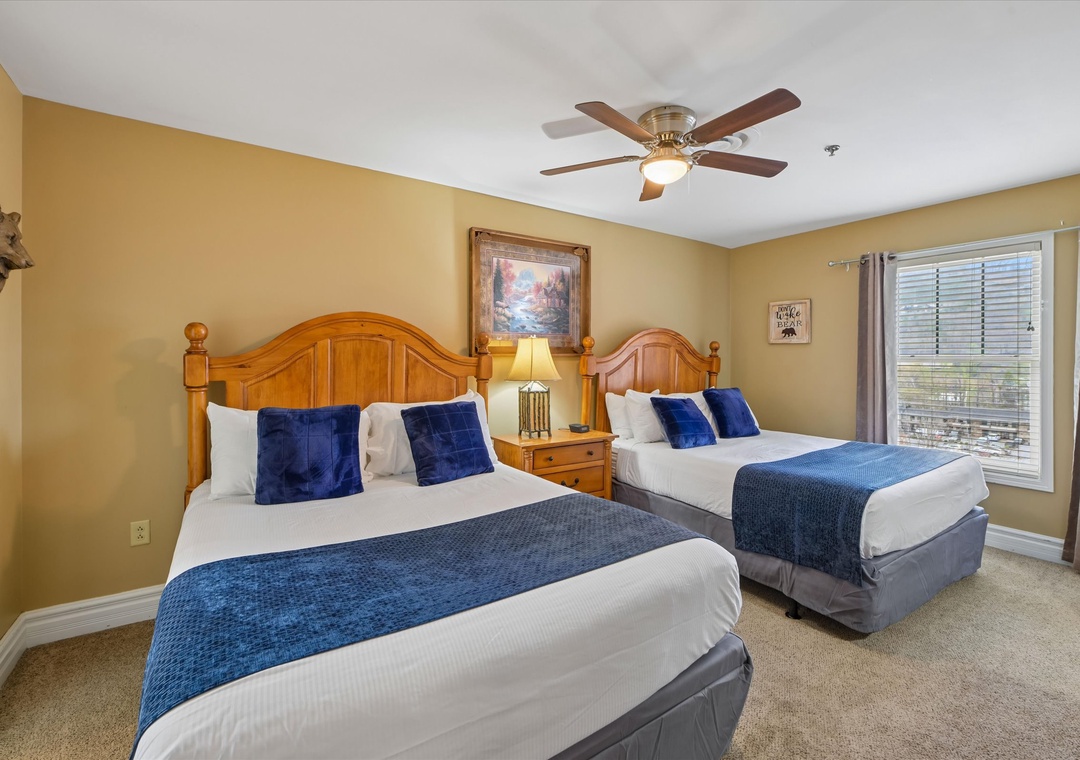 Two comfortable beds with crisp linens and blue accents await you in this warm, welcoming bedroom with a ceiling fan for your comfort.
