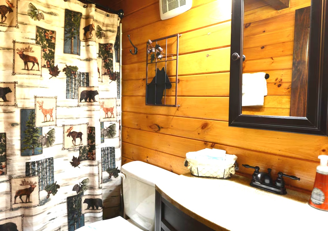 Rustic charm meets comfort in your cabin bathroom, with warm wood walls, wildlife-themed curtains, and fluffy towels ready for your relaxing soak.