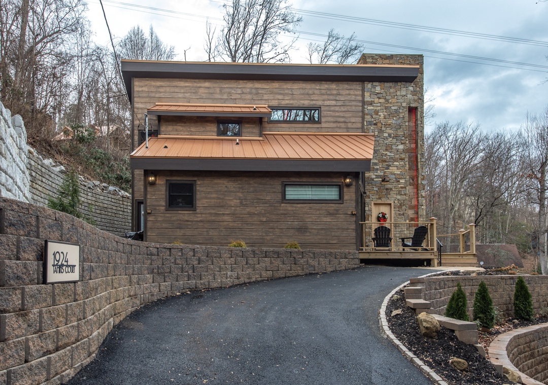 Modern retreat featuring natural wood and stone architecture, nestled among bare winter trees with curved driveway access.