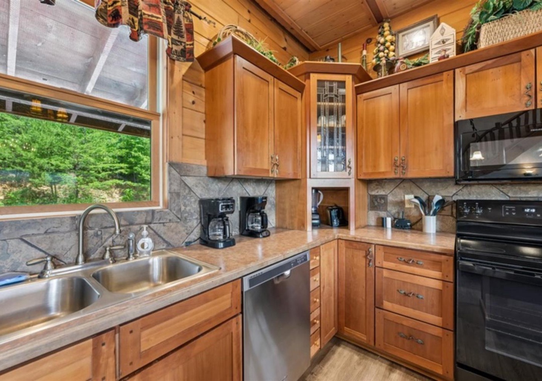 Your cabin-style kitchen boasts rich wood cabinetry, modern appliances, and a bright window overlooking lush greenery—perfect for brewing morning coffee and enjoying nature's beauty while you prepare meals.