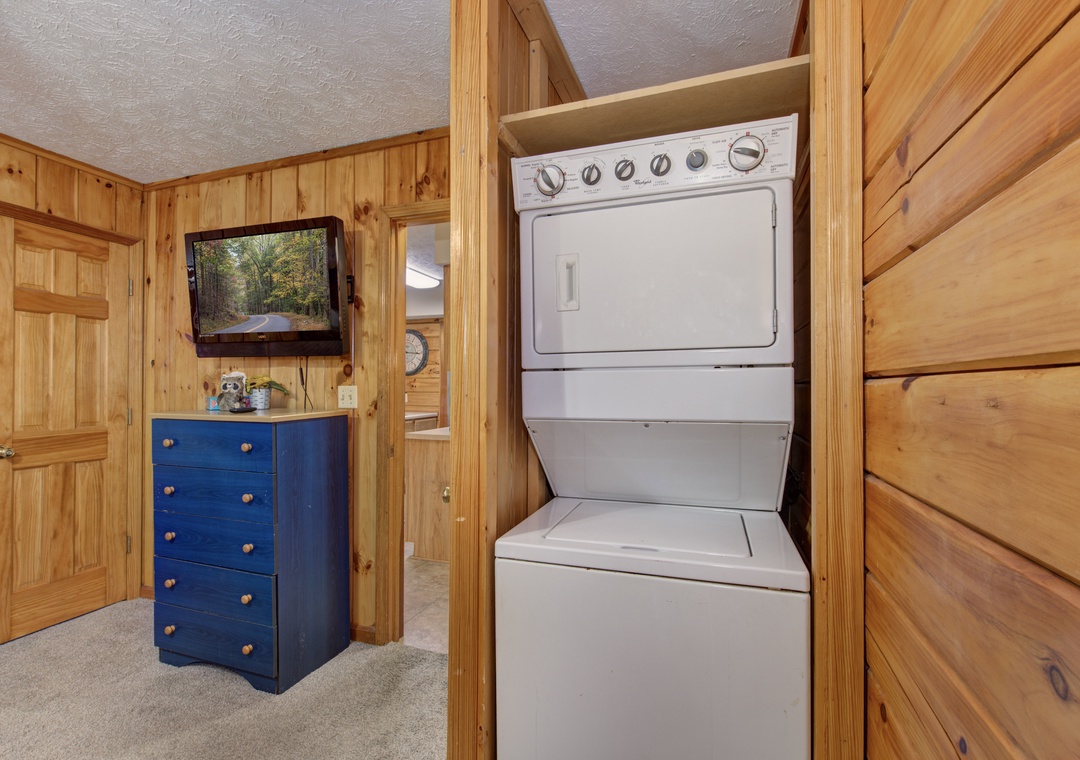 Your convenient laundry setup and entertainment area await, featuring stacked washer-dryer and charming blue storage with mounted TV for relaxing while clothes wash.