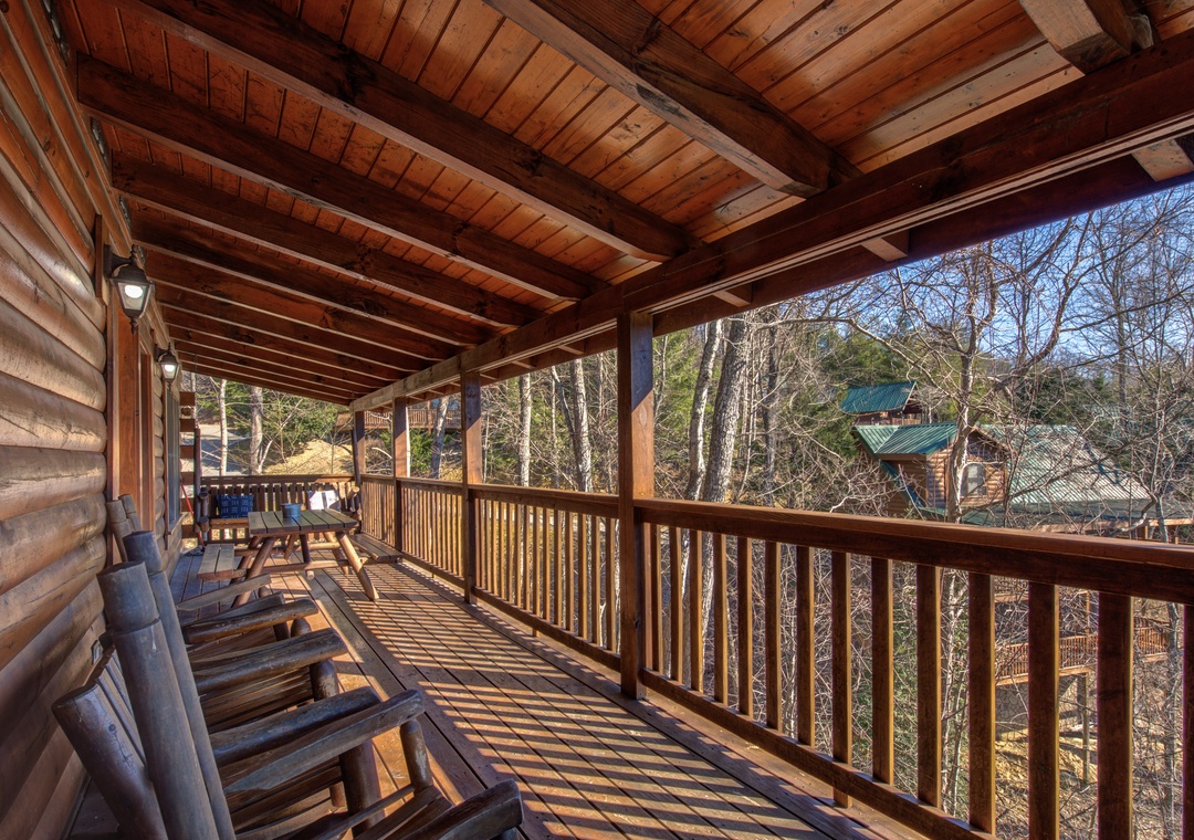 Relax on your private covered balcony with rustic wooden beams overhead and peaceful forest views stretching beyond the railing.