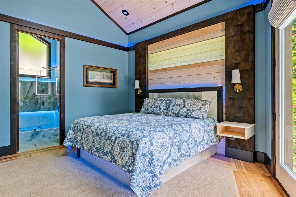 Your serene bedroom retreat features calming blue tones, rustic wood accents, and a plush bed awaiting your arrival. Step into your private en-suite through the doorway.