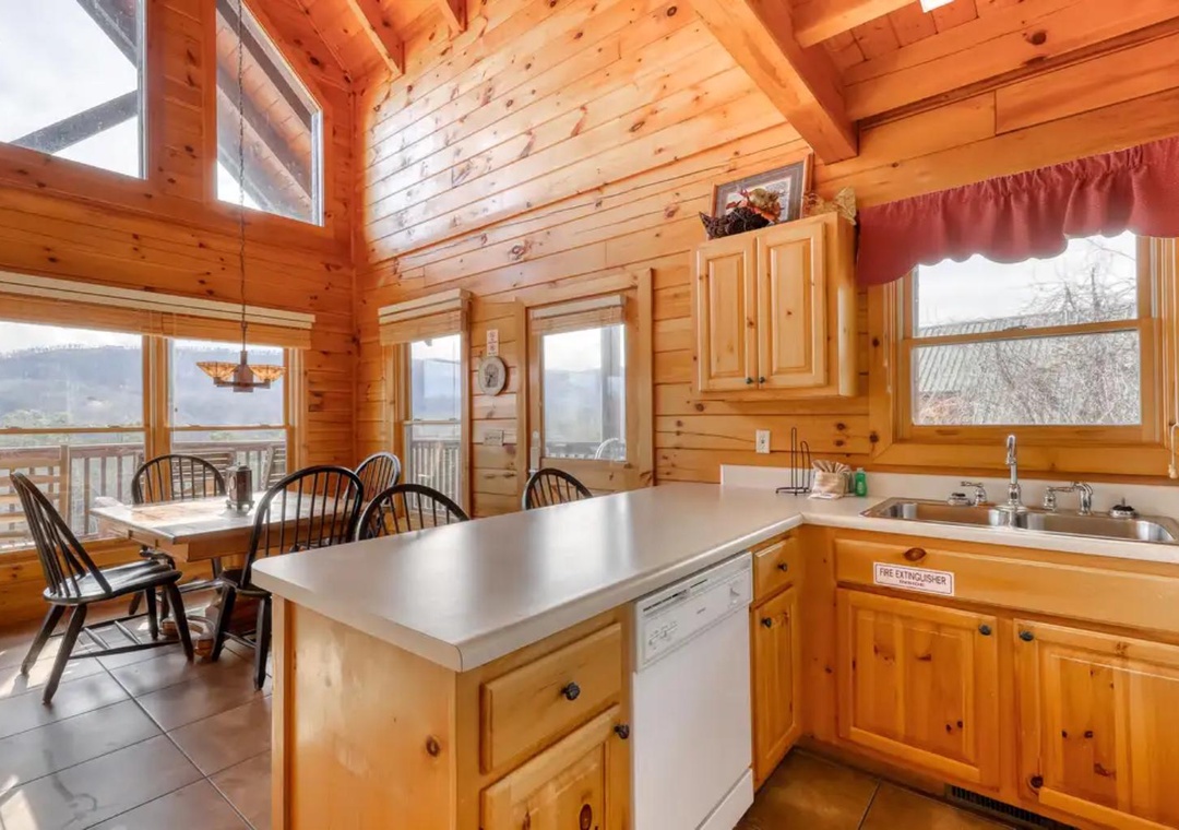 Bright, open-plan kitchen and dining area with warm wood, vaulted ceilings, and tall windows framing stunning mountain views—the perfect gathering place for memorable meals.