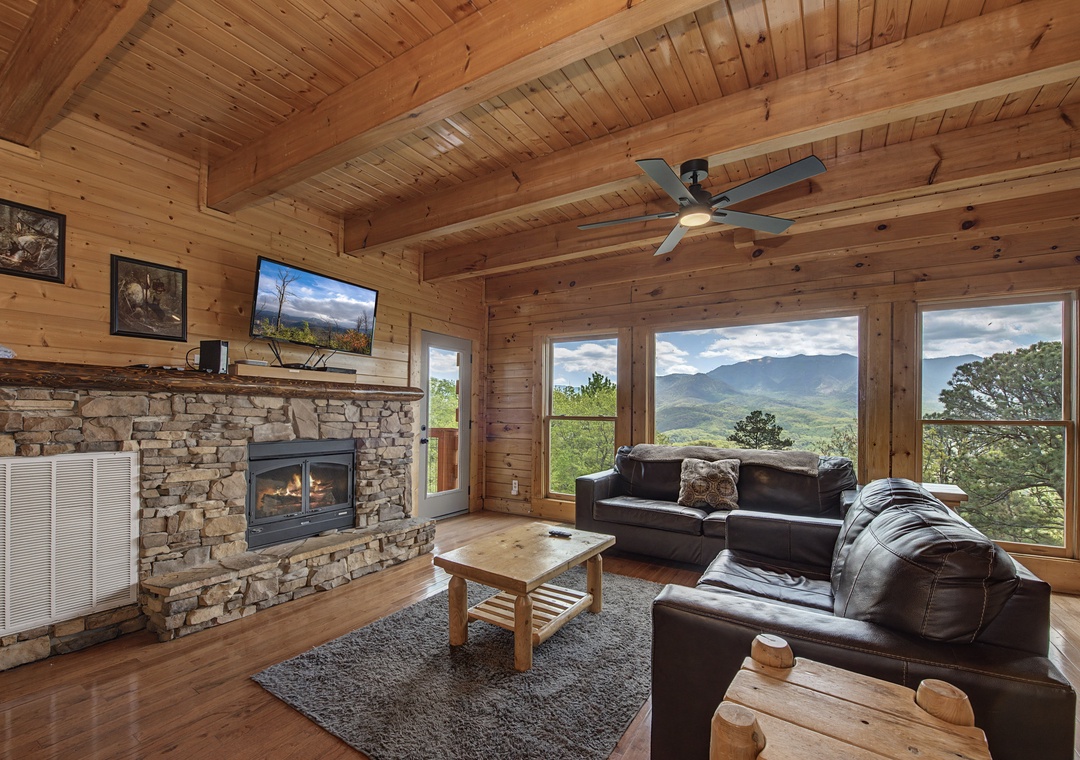 Relax in this cozy mountain cabin living room with panoramic views, stone fireplace, and rustic charm perfect for your getaway.