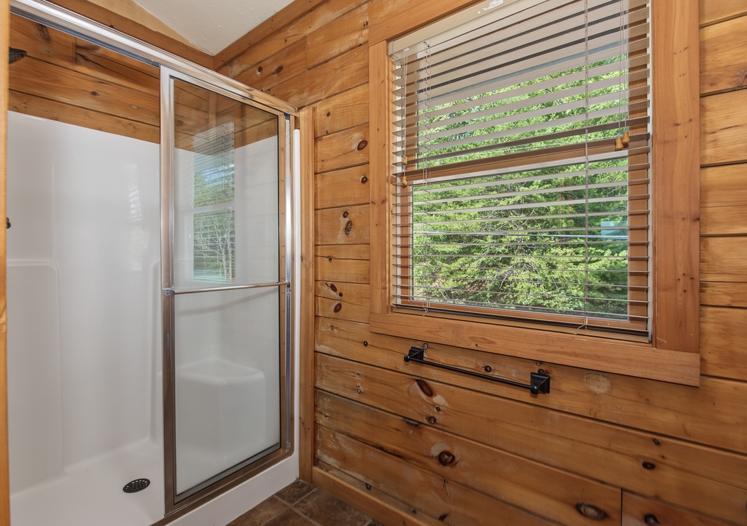 Step into your private bathroom featuring warm wood walls and a clean, modern shower. Natural light filters through the window, bringing the surrounding greenery right to your space.