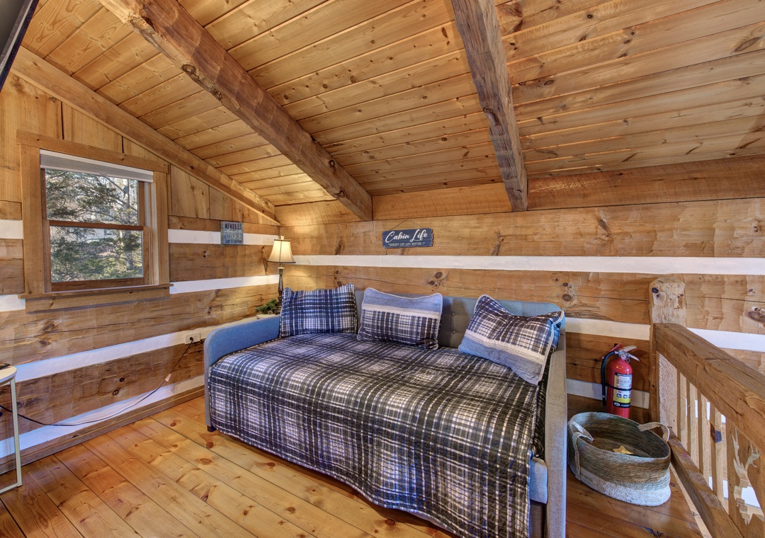 Your cozy loft bedroom features warm wood beams and plaid bedding for restful mountain nights.