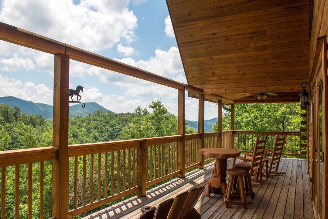 Mountain views surround your private covered deck, where wooden seating awaits your morning coffee or evening wine. The lush forest below adds to the peaceful mountain retreat atmosphere.