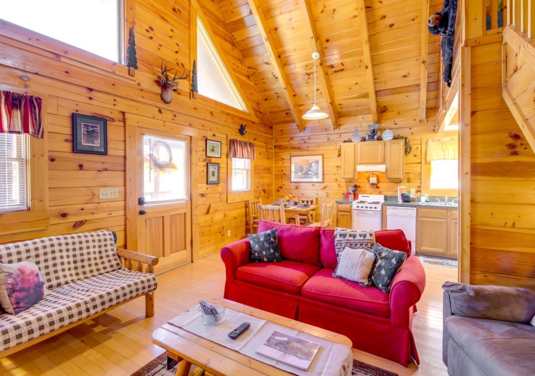 Settle into your cozy log cabin retreat with exposed beams, warm wood walls, and a vibrant red sofa perfect for evening relaxation.