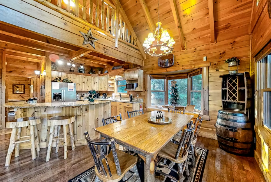 Gather around the rustic dining table in your cozy log cabin, where warm wood surrounds you and the loft above creates intimate charm.